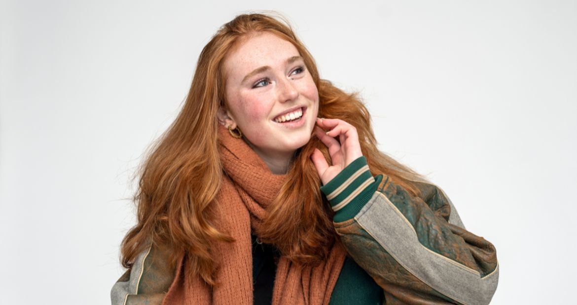 Mulher sorrindo com a mão encostando em seu rosto com cabelo em tom ruivo nude.